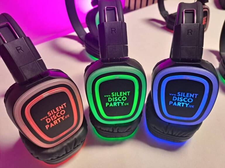 Three Silent Disco Party UK wireless headphones lined up showing red, green and blue LED channel lights glowing in the dark